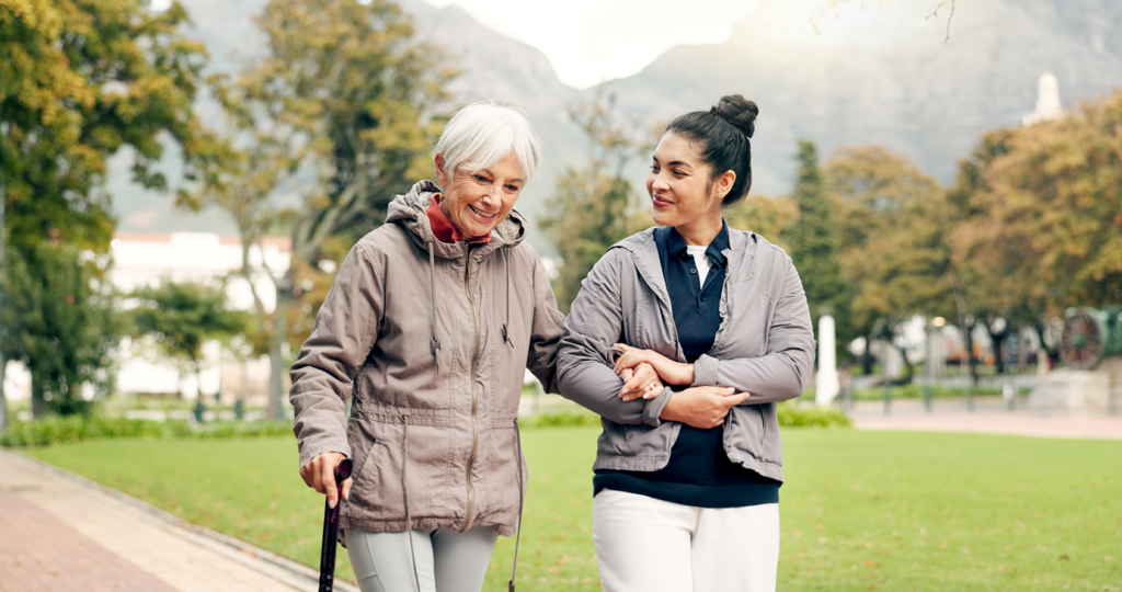 Elderly woman with cane walking arm-in-arm with aged care facility nurse