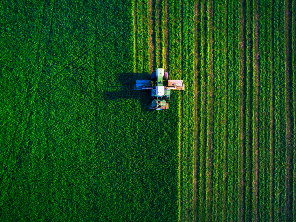 A tractor plowing a lush green field from above.