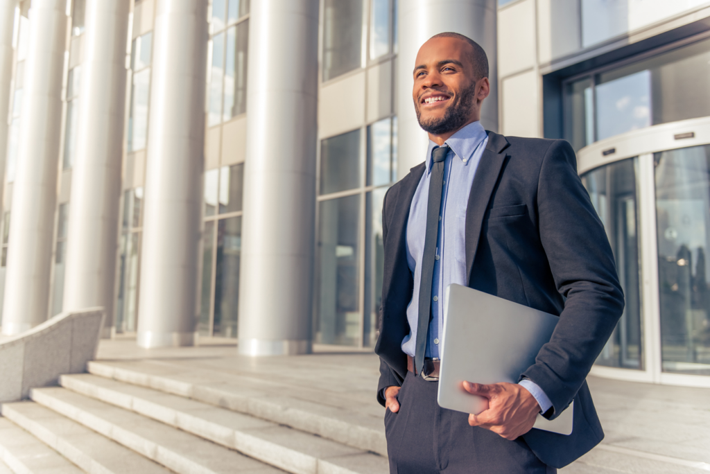 Business man exiting a corporate office building holding laptop