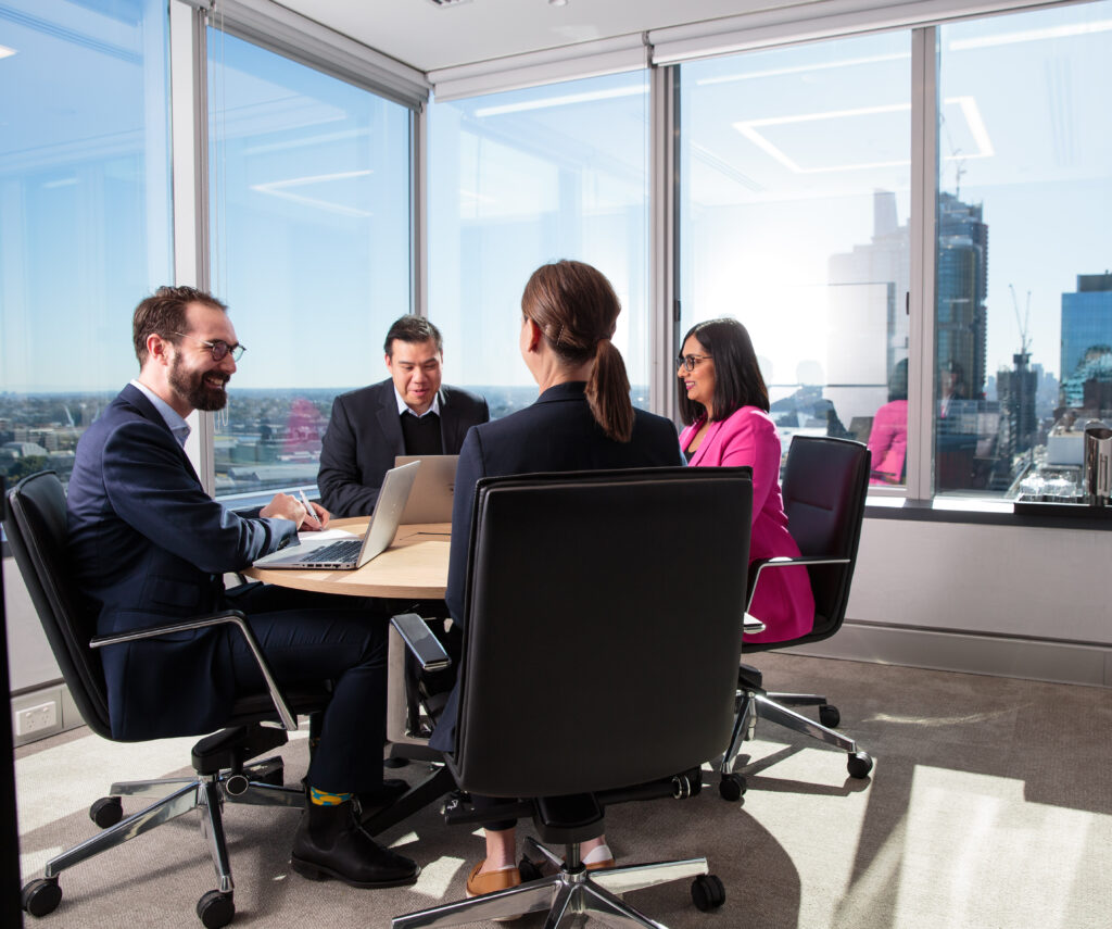 four people in meeting room at round table working and smiling